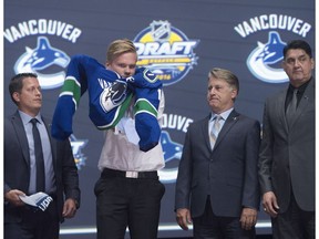 Olli Juolevi, fifth overall pick, puts on his sweater as he stands on stage with members of the Vancouver Canucks management team at the 2016 NHL draft in Buffalo.
