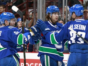 Vancouver Canucks blueliners Troy Stecher (left) and Ben Hutton, shown celebrating a goal with Henrik Sedin earlier this season, have broken into the team’s lineup over the last two seasons straight out of U.S. college hockey.