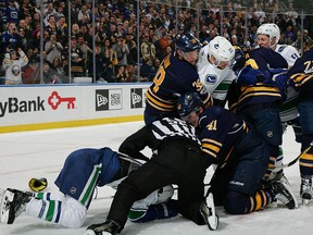 Justin Falk and Alex Burrows are separated by linesman Shandor Alphonsos.