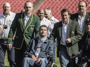 Rugby World Cup winning team captain Francois Pienaar (lest) assisted his former teammate Joost van der Westhuizen during a re-enactement of the team photo from the 1995 Rugby World cup victory on June 24, 2015 at Ellis Park in Johannesburg.