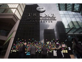 People stop to read messages written by protesters posted on the wall outside the official opening of the Trump International Hotel and Tower in Vancouver, B.C., on Tuesday, February 28, 2017. U.S. President Donald Trump's sons Donald Jr. and Eric attended the opening.