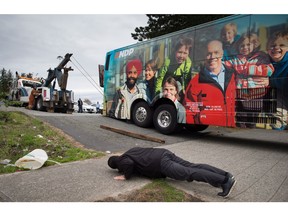 The driver of a relief bus that was called in watches as a tow truck operator tries to free NDP Leader John Horgan's campaign bus after it became stuck while trying to exit a parking lot in Surrey, B.C., on Monday May 8, 2017.