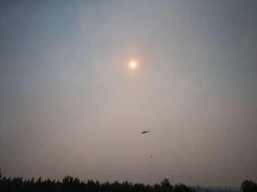 Smoke obscures the sun as a helicopter carrying a bucket battles the Gustafsen wildfire near 100 Mile House, B.C., on Saturday July 8, 2017.