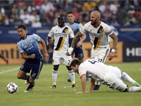 Vancouver Whitecaps forward Nicolas Mezquida, left, moves the ball ahead of Los Angeles Galaxy defenders Jelle Van Damme and defender Dave Romney  during the first half at StubHub Center in July 2017.