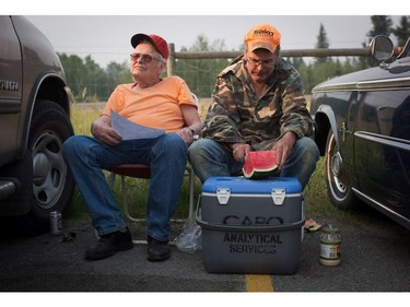 Floyd Lee, right, cuts watermelon while sitting with his father Garth Lee, both evacuated from their homes in 108 Mile Ranch, while sitting in the parking lot outside a curling club being used as an evacuation centre in 100 Mile House, B.C., on Saturday July 8, 2017.