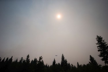 Smoke obscures the sun as a helicopter carrying a bucket battles the Gustafsen wildfire near 100 Mile House, B.C., on Saturday July 8, 2017.