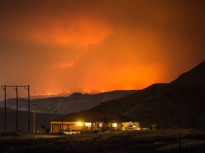 A wildfire burns on a mountain in the distance east of Cache Creek behind a house in Boston Flats, B.C., in the early morning hours of Monday July 10, 2017.
