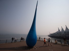 Smoke from wildfires burning in central B.C. hangs in the air as people look out at the harbour from a viewpoint where a steel sculpture of a raindrop stands, in Vancouver, on Aug. 10, 2017.