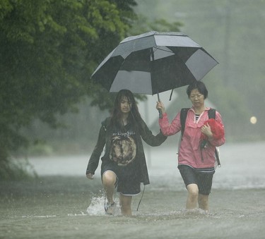 Two woman walk in heavy rain as they evacuate floodwaters from Tropical Storm Harvey on Sunday, Aug. 27, 2017, in Houston, Texas.