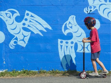 A boy rides past a mural by Khelsilem at the Vancouver Mural Festival held in Mount Pleasant, Vancouver.
