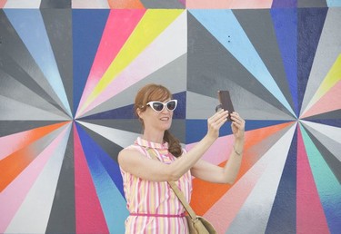 A woman takes a selfie in front of a mural by Jane Cheng at the Vancouver Mural Festival held in Mount Pleasant, Vancouver.