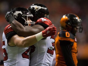 Calgary Stampeders' Rob Cote (left) and Jerome Messam celebrate Messam's touchdown as the B.C. Lions' Loucheiz Purifoy (back right) walks to the sideline during the second half of their Canadian Football League game at B.C. Place Stadium on Aug. 18, 2017. The Stampeders won 21-17.