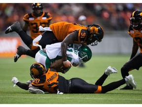 Myke Tavarres of the Saskatchewan Roughriders, centre, is tackled by B.C. Lions' Micah Awe, top, and Keynan Parker earlier this season.