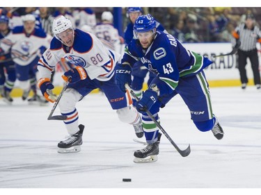 Vancouver Canucks Jonah Gadjovich gives chase to the loose puck while pressured by Edmonton Oilers Austin Strand.