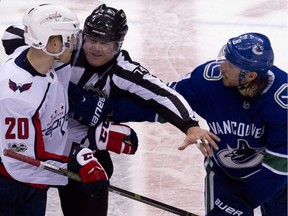 Linesman Lonnie Cameron, centre gets between Washington Capitals' Lars Eller, left and Vancouver Canucks' Chris Tanev, right at the end of an NHL hockey game in Vancouver, B.C., on Thursday October 26, 2017.