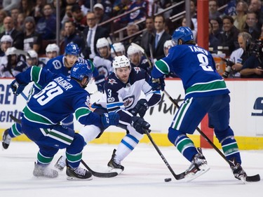 Winnipeg Jets' Tucker Poolman, centre, tries to skate with the puck past Vancouver Canucks' Sam Gagner, left, and Chris Tanev during the first period of an NHL hockey game in Vancouver, B.C., on Thursday October 12, 2017.