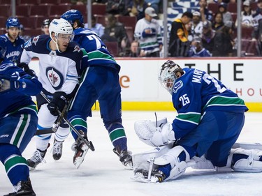 Vancouver Canucks' goalie Jacob Markstrom, right, of Sweden, makes the save as Winnipeg Jets' Shawn Matthias, left, looks for the rebound while being checked by Vancouver's Ben Hutton during the first period of an NHL hockey game in Vancouver, B.C., on Thursday October 12, 2017.