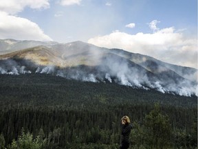 A woman stops on the side of the highway to watch a forest fire burn near Revelstoke on Aug. 19.