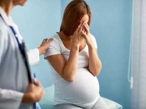 Stressed pregnant female hiding her face by palms while clinician sympathizing her