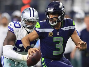 Russell Wilson of the Seattle Seahawks runs away from DeMarcus Lawrence of the Dallas Cowboys in the second half at AT&T Stadium on December 24, 2017 in Arlington, Texas.