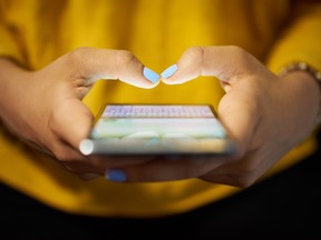 DIRECTINPUT~  This image has been directly inputted by the user. The photo desk has not viewed this image or cleared rights to the image. Young woman using cell phone to send text message on social network at night. Closeup of hands with computer laptop in background

		diego_cervo / iStock / Getty Images Plus