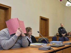 FILE - In this Feb. 26, 2015 file photo former nurse Niels Hoegel, accused of multiple murder and attempted murder of patients, covering his face with a file at the district court in Oldenburg, Germany. The German nurse already serving a life sentence for two murders has been indicted in nearly 100 more killings. News agency dpa said prosecutors in Oldenburg said Monday, Jan. 22, 2018 that they have charged Niels Hoegel with 97 counts of murder. (Carmen Jaspersen/dpa via AP, file) ORG XMIT: LGL101