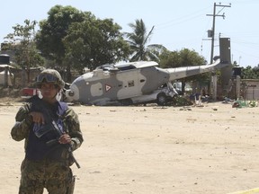 A soldier guards a downed helicopter in Santiago Jimitepec, Oaxaca state, Mexico, Saturday, Feb. 17, 2018. The military helicopter carrying officials assessing damage from the Friday's earth quake crashed killing 13 people and injuring 15, all of them on the ground.