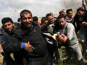 An injured Palestinian man is carried by fellow protesters as they run for cover during clashes with Israeli security forces following a demonstration commemorating Land Day near the border with Israel, east of Khan Yunis, in the southern Gaza Strip on March 30, 2018.