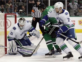 Jacob Markstrom traps a puck beneath his leg pad as defenceman Alexander Edler helps against pressure from the Stars' Curtis McKenzie.