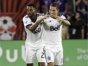Vancouver Whitecaps's Aaron Maund, left, and Nicolas Mezquida celebrate after Orlando City scored an own goal during a 2017 game in Orlando, Fla.