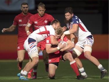 Ben Pinkelman and Danny Barrett of the United States try to gain control of the ball from Canada's John Moonlight during a match at the World Rugby Seven Series at B.C. Place in Vancouver, Saturday, March, 10, 2018.