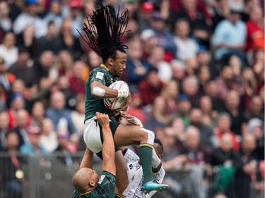 South Africa's Cecil Afrika, top, is lifted by Zain Davids, left, as he grabs the ball away from Fiji's Sevuloni Mocenacagi, back, during World Rugby Sevens Series action, in Vancouver, B.C., on Sunday March 11, 2018.