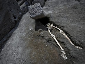 The legs of a skeleton emerge from the ground beneath a large rock believed to have crushed the victim's bust during the eruption of Mt. Vesuvius in A.D. 79, which destroyed the ancient town of Pompeii, at Pompeii's archeological site, near Naples, on Tuesday, May 29, 2018.