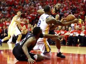 Andre Iguodala (in white) of the Golden State Warriors runs interference on the ball between guards James Harden (on the floor) and Chris Paul (right) of the Houston Rockets during Game 1 of the NBA Western Conference finals at Houston’s Toyota Center on May 14, 2018.
