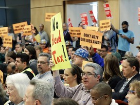 In this Wednesday, May 9, 2018 file photo opponents and supporters of a controversial proposal to tax large businesses such as Amazon.com to fund efforts to combat homelessness hold signs at City Hall in Seattle.