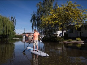 Trudy Johnston uses a stand up paddleboard to navigate the flooded street in her neighbourhood as water from Osoyoos Lake floods the street and properties, in Osoyoos, B.C., on Saturday May 12, 2018. Thousands of people have been evacuated from their homes in British Columbia's southern interior as officials warn of flooding due to extremely heavy snowpacks, sudden downpours and unseasonably warm temperatures.