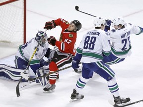Chicago Blackhawk Tanner Kero (in red) takes it on the chin from a high stick courtesy of Vancouver Canucks blueliner Ben Hutton (right) as Nikita Tryamkin and goalie Ryan Miller also defend during a March 2017 NHL game at the United Center in Chicago.