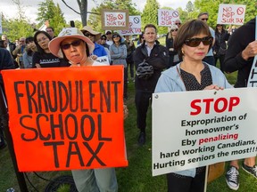 Demonstrators hold signs at an anti-school tax rally before a town hall meeting organized by local MLA David Eby in Vancouver Monday night.