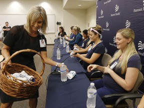 Banner Desert Medical Center CEO Laura Robertson, left, hands out baby outfits Friday, Aug. 17, 2018, in Mesa, Ariz., to the sixteen pregnant nurses who work together in the intensive care unit at Banner Desert Medical Center at a news conference where they all talk about all being pregnant at the same time, with most of them due to give birth between October and January.