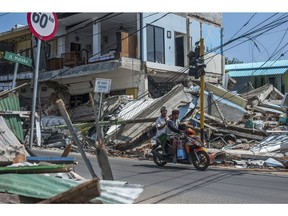 In this Friday, Aug. 10, 2018, photo, motorists ride past buildings ruined by Sunday's earthquake in Pamenang, Lombok Island, Indonesia. The north of the popular resort island has been devastated by Sunday's earthquake, damaging thousands of buildings and killing a large number of people.
