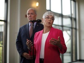 B.C. Premier John Horgan looks on as Finance Minister Carole James answers a question during a media scrum following a meeting with federal ministers at the Vancouver Island Conference Centre during day two of the Liberal cabinet retreat in Nanaimo, B.C., on Wednesday, August 22, 2018. British Columbia maintained its budget surplus in the last fiscal year even though it boosted spending on government programs by almost $3 billion and covered significant expenses from disastrous wildfires in 2017.