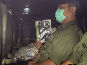 In this Sept. 19, 2018 photo, Malaysian citizen Khaw Kim Sun, 53, center, covered face, is escorted in a prison bus leaving the court after sentenced to life in prison in Hong Kong. Kim, an anesthesiologist convicted of killing his wife and daughter by placing a yoga ball that leaked carbon monoxide in their car has been sentenced to life in prison in Hong Kong. (Apple Daily via AP) ORG XMIT: HK901