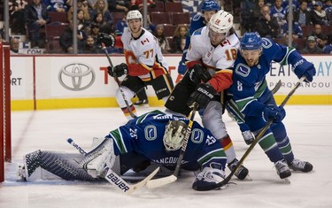 Goalie Jacob Markstrom #25 of the Vancouver Canucks looks to cover up the loose puck while James Neal #18 of the Calgary Flames and Chris Tanev #8 of the  Canucks battle in NHL action on October, 3, 2018 at Rogers Arena in Vancouver, British Columbia, Canada.