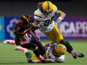 B.C. Lions' Chris Rainey is taken down by then-Edmonton Eskimo Aaron Grymes, top, and Adam Konar during a CFL game in Vancouver on Oct. 21, 2017.