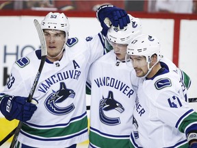 Vancouver Canucks' Bo Horvat, left, celebrates his goal with teammates Elias Pettersson, centre, and Sven Baertschi during NHL action against the Flames in Calgary on Oct. 6.