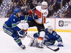 Canucks defenseman Michael Del Zotto tries to clear Calgary Flames centre Mikael Backlund from in front of goaltender Jacob Markstrom.