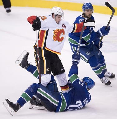 Vancouver Canucks defenseman Christopher Tanev (8) looks on as Calgary Flames center Sean Monahan (23) fights for control of the puck with Vancouver Canucks defenseman Alexander Edler (23) during third period NHL action at Rogers Arena in Vancouver, Wednesday, Oct, 3, 2018.