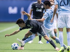 Vancouver Whitecaps' Nicolas Mezquida, left, and Sporting Kansas City's Roger Espinoza vie for the ball during the first half of an MLS soccer game in Vancouver, on Wednesday October 17, 2018.