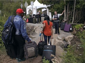 In this Aug. 7, 2017 file photo, a RCMP officer informs a migrant couple of the location of a legal border station, shortly before they illegally crossed from Champlain, N.Y., to Saint-Bernard-de-Lacolle, Quebec, using Roxham Rd.