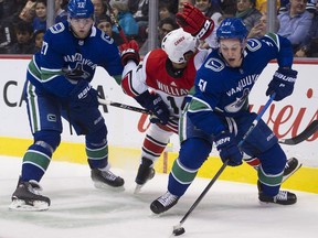Canucks defenceman Troy Stecher looks to clear the puck as teammate Ben Hutton pressures Carolina Hurricane Justin Williams.